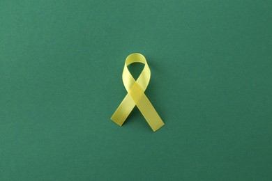 Photo of Yellow awareness ribbon on green background, top view
