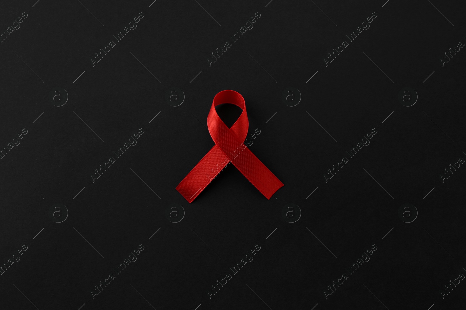 Photo of Red awareness ribbon on black background, top view