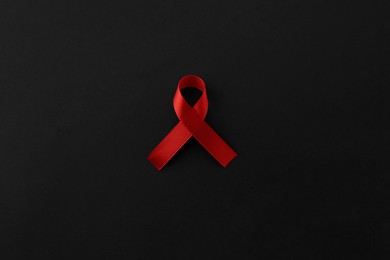 Photo of Red awareness ribbon on black background, top view