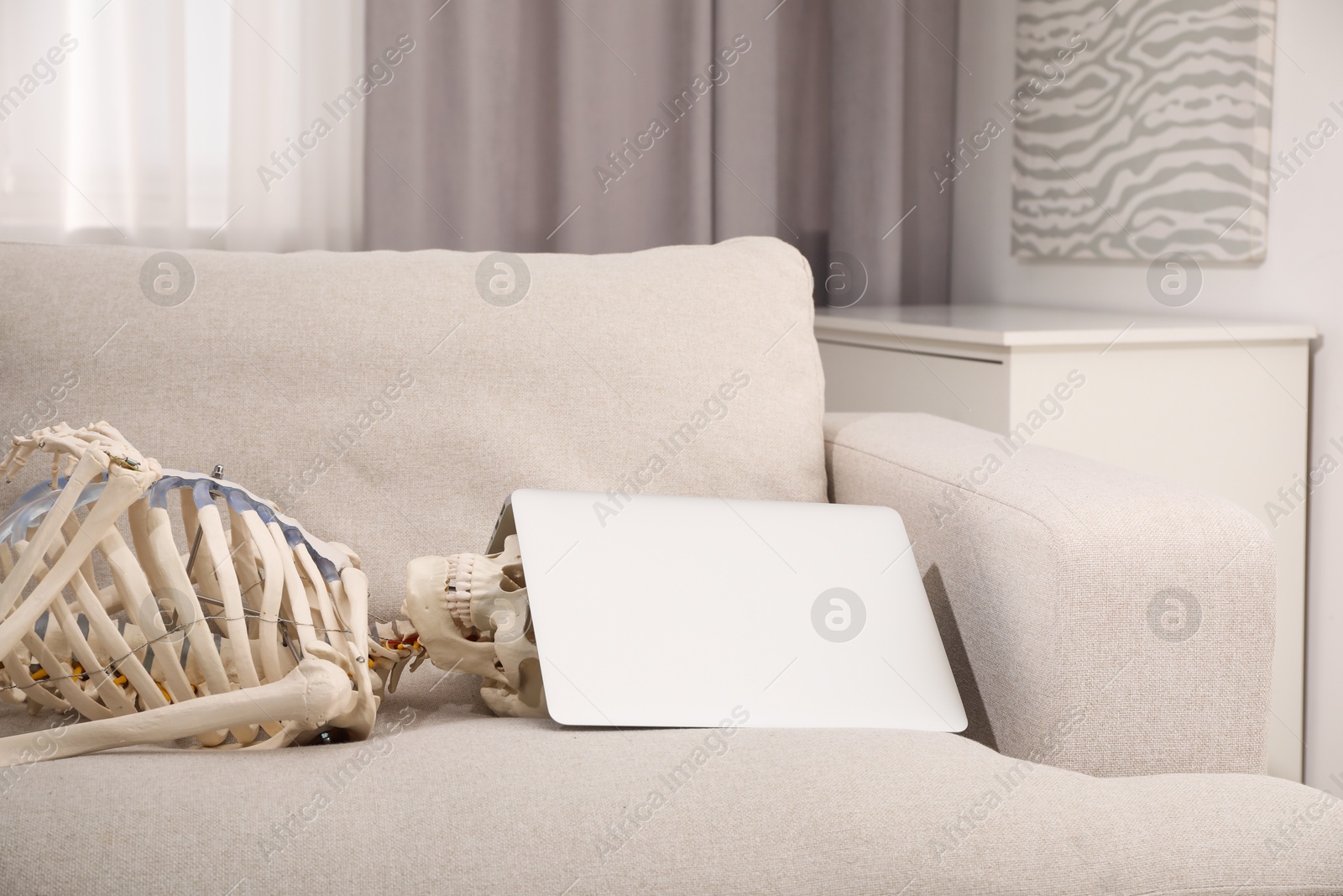 Photo of Waiting concept. Human skeleton with laptop on sofa
