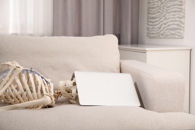 Waiting concept. Human skeleton with laptop on sofa