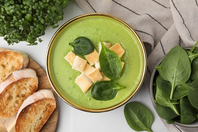 Photo of Delicious spinach cream soup with croutons in bowl on white tiled table, flat lay