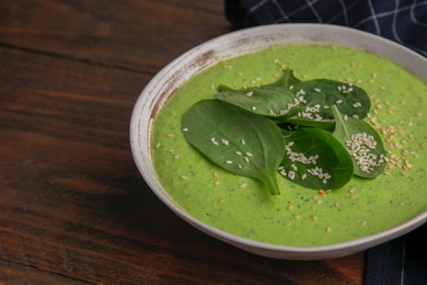 Photo of Delicious spinach cream soup with fresh leaves and sesame seeds in bowl on wooden table, closeup. Space for text