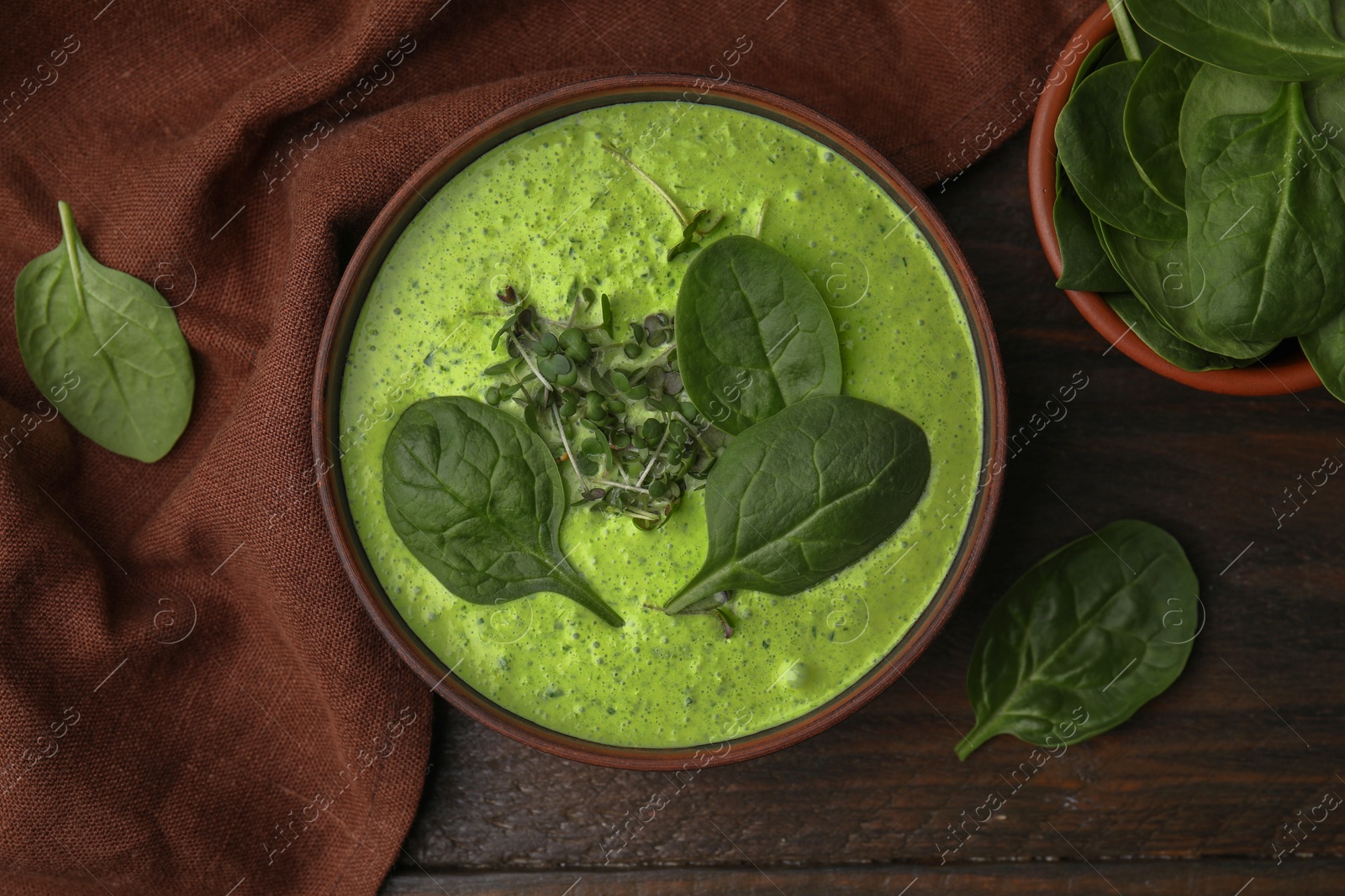 Photo of Delicious spinach cream soup with fresh leaves and microgreens in bowl on wooden table, flat lay