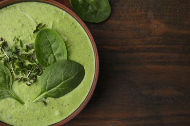 Photo of Delicious spinach cream soup with fresh leaves and microgreens in bowl on wooden table, top view. Space for text