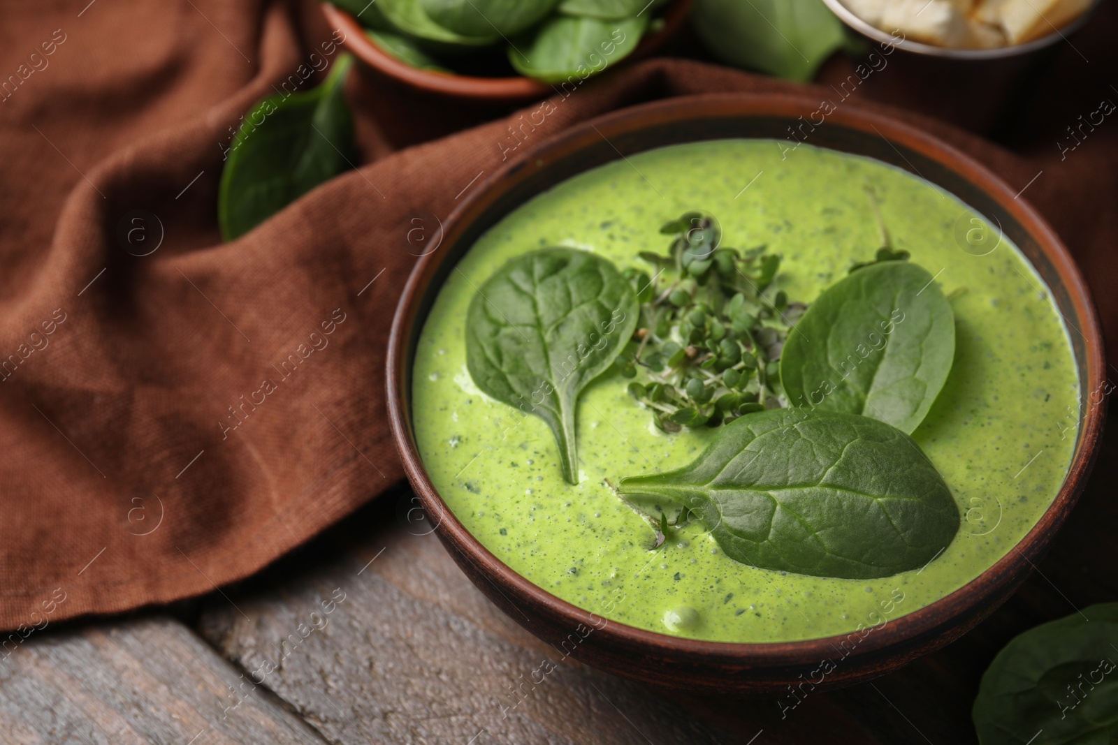 Photo of Delicious spinach cream soup with fresh leaves and microgreens in bowl on wooden table, closeup