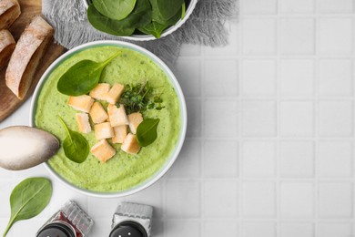 Photo of Delicious spinach cream soup with croutons served on white tiled table, flat lay. Space for text