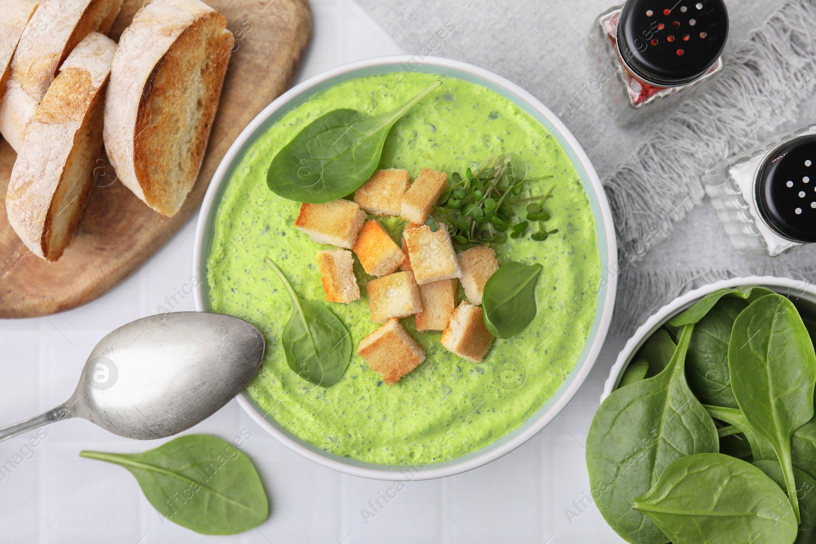 Photo of Delicious spinach cream soup with croutons served on white tiled table, flat lay