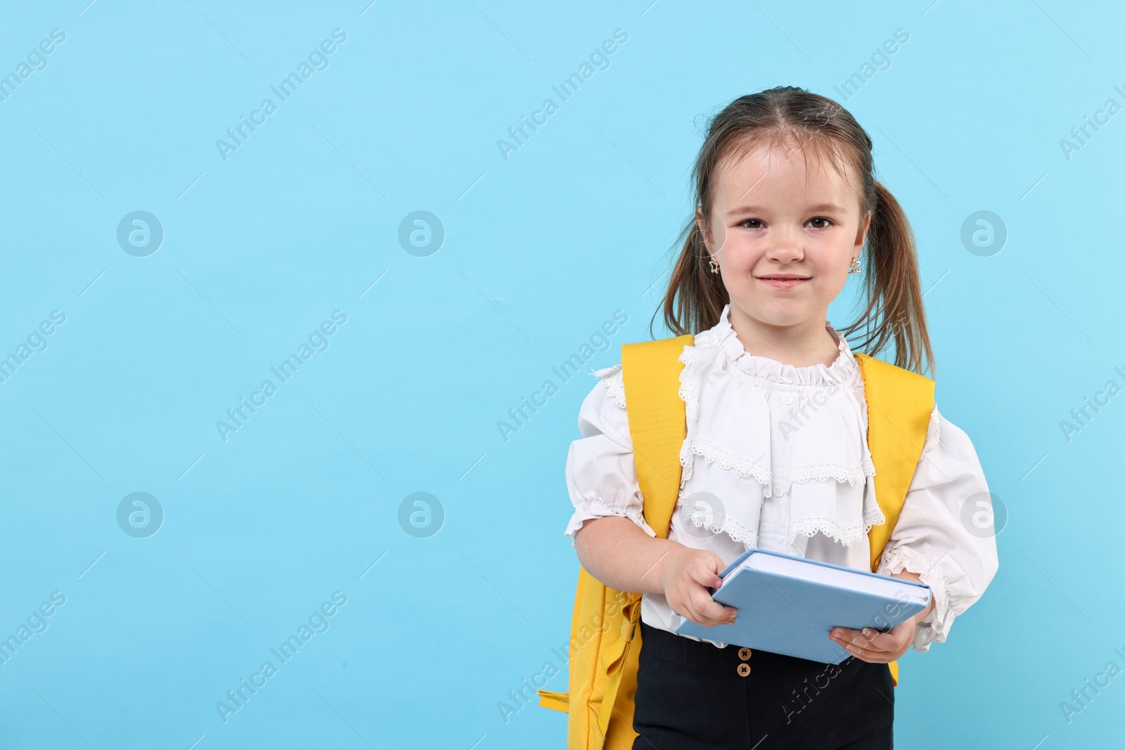 Photo of Cute little girl with book and backpack on light blue background. Space for text