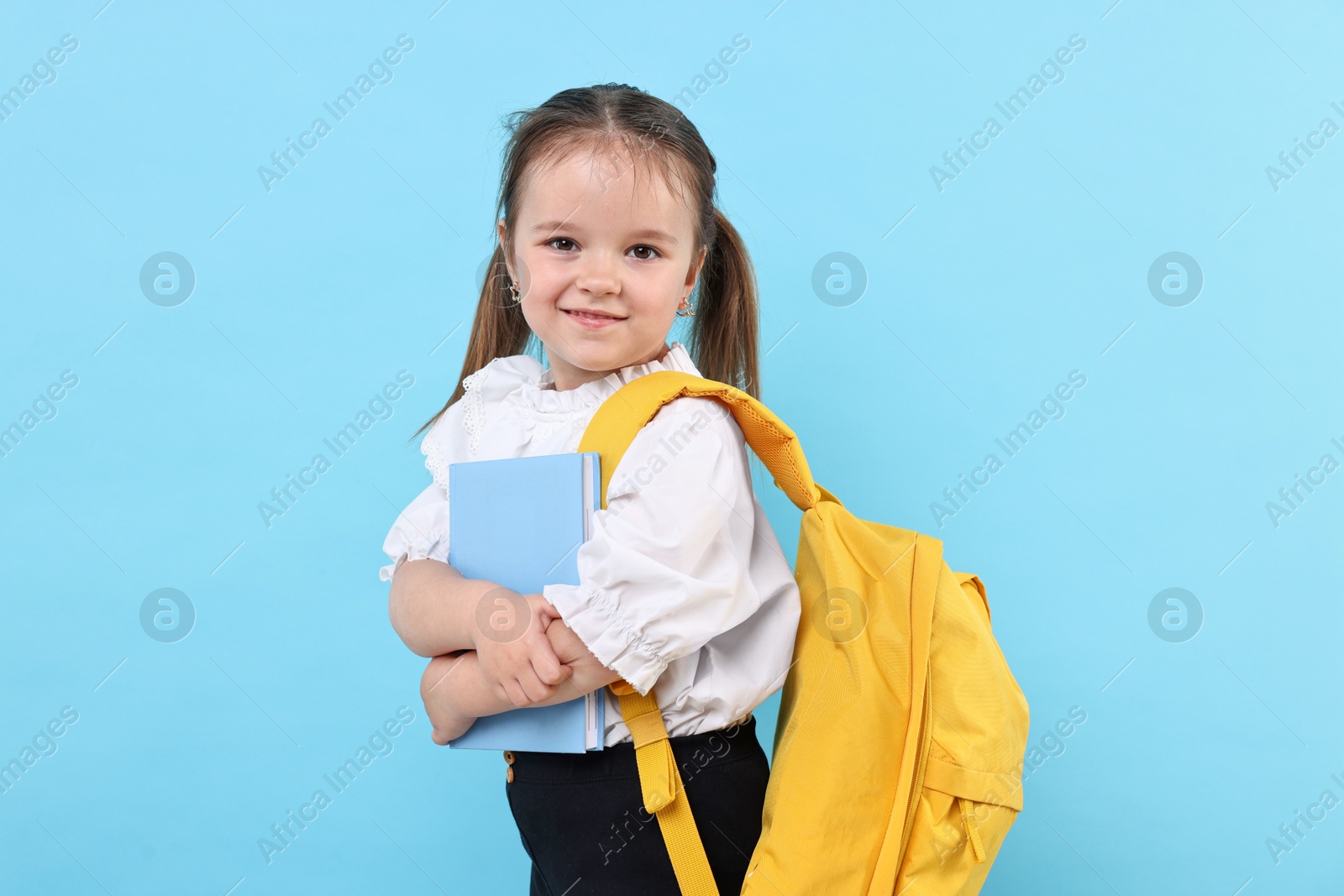 Photo of Cute little girl with book and backpack on light blue background
