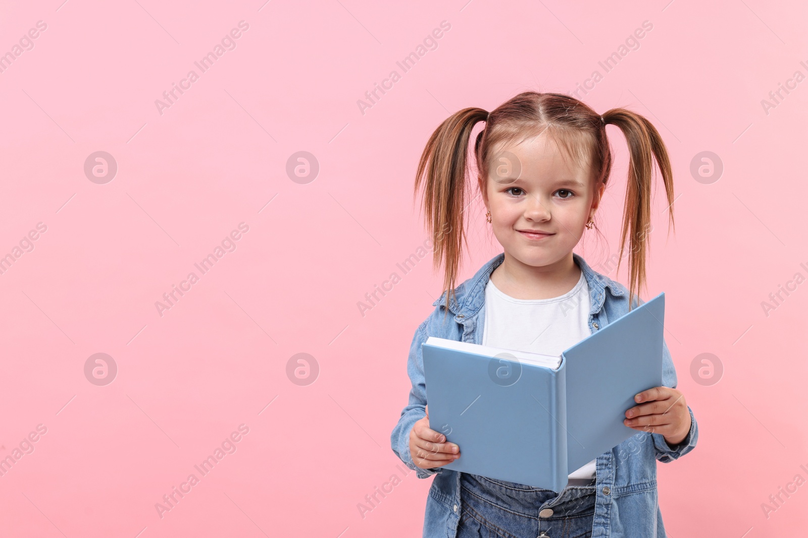Photo of Cute little girl with book on pink background. Space for text