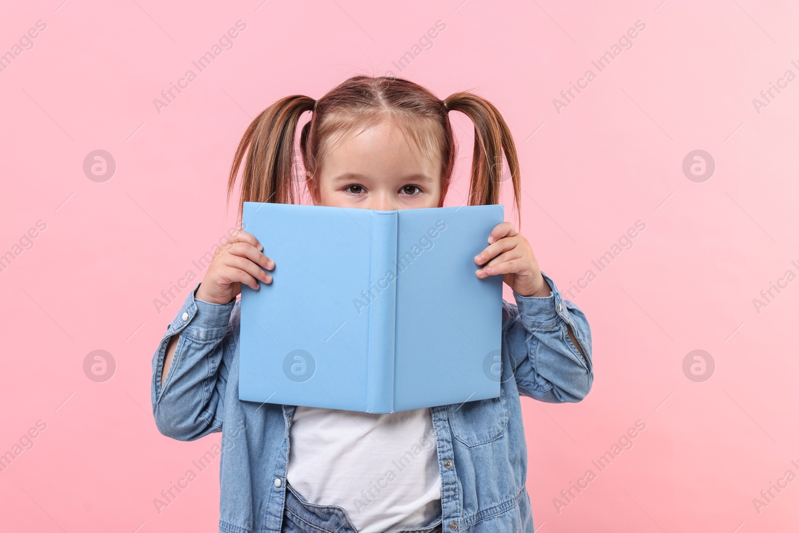 Photo of Cute little girl with open book on pink background