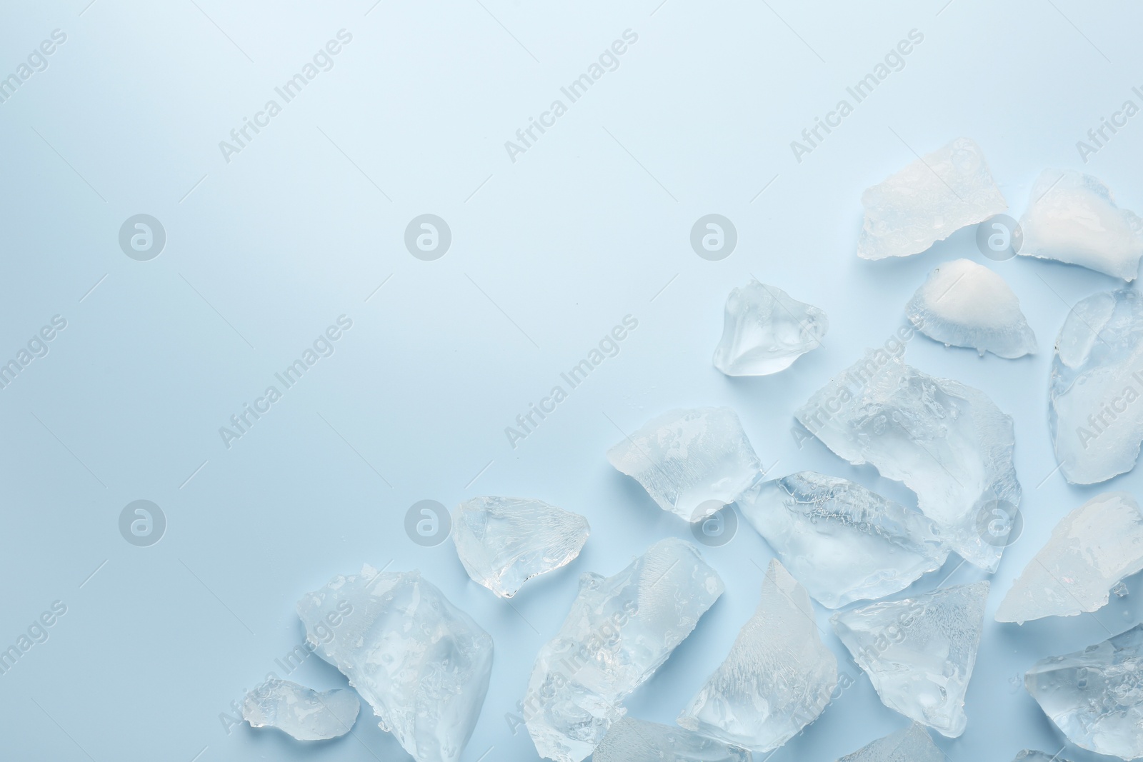 Photo of Pieces of crushed ice on light blue background, top view. Space for text