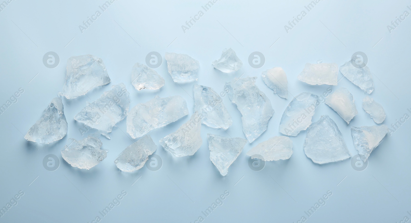 Photo of Pieces of crushed ice on light blue background, top view