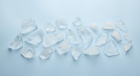 Pieces of crushed ice on light blue background, top view