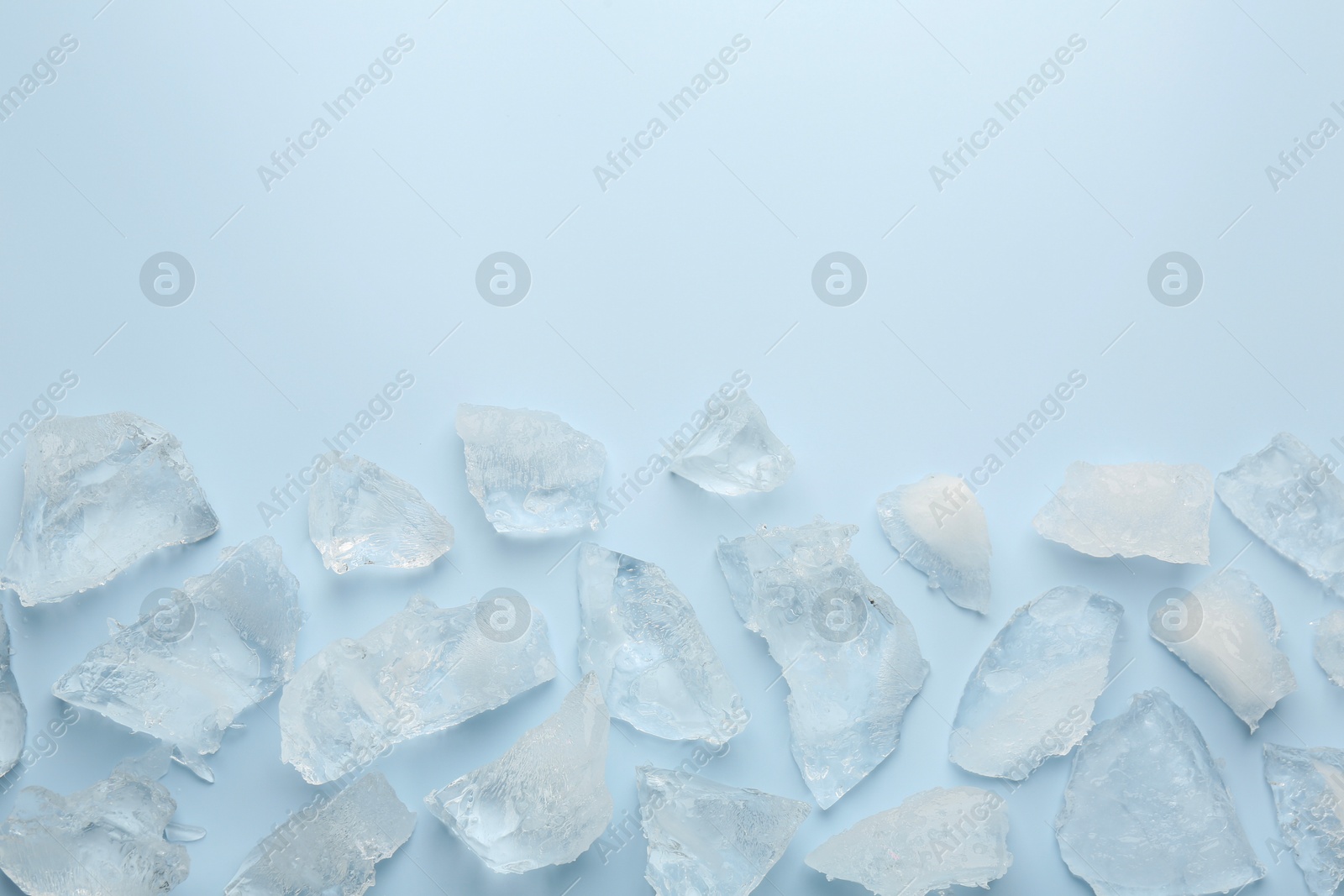 Photo of Pieces of crushed ice on light blue background, top view. Space for text