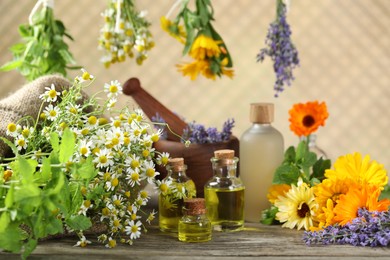 Photo of Different flowers, bottles of essential oils, mint mortar and pestle on wooden table