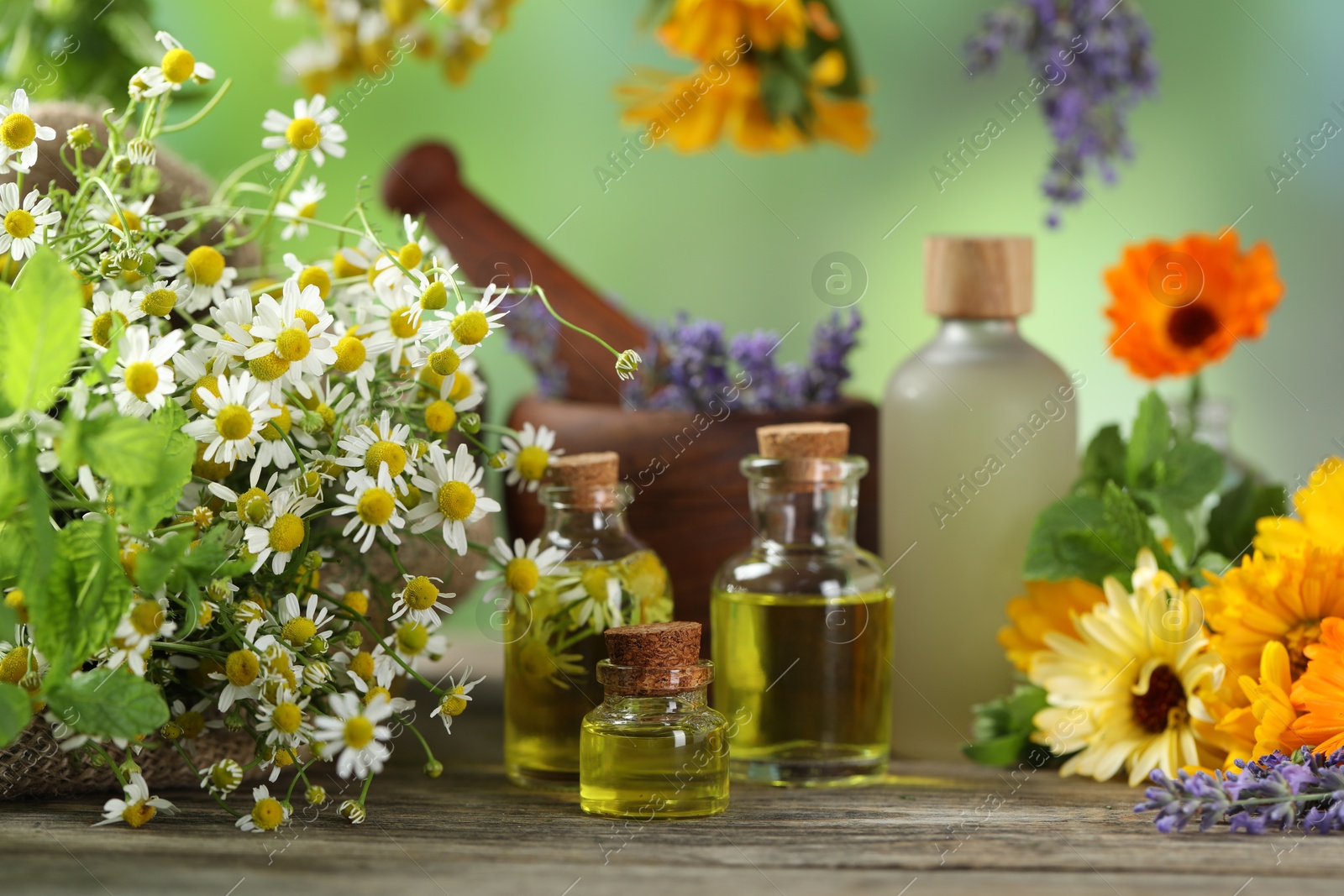 Photo of Different flowers, bottles of essential oils, mint mortar and pestle on wooden table