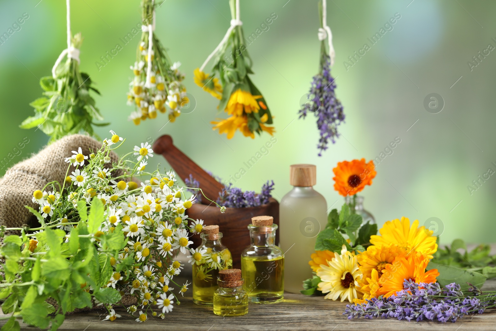 Photo of Different flowers, bottles of essential oils, mint mortar and pestle on wooden table