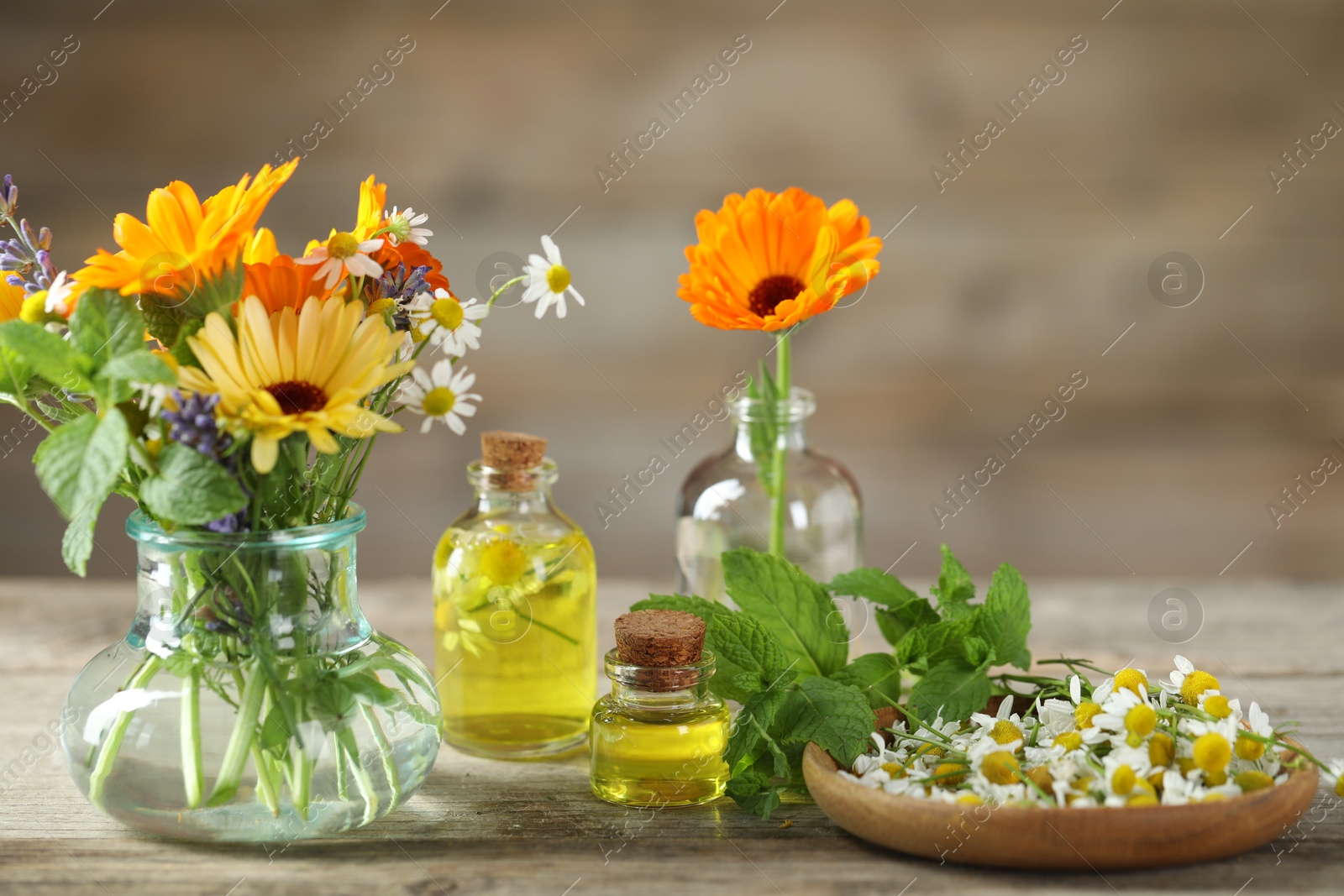 Photo of Different flowers, mint and bottles of essential oils on wooden table