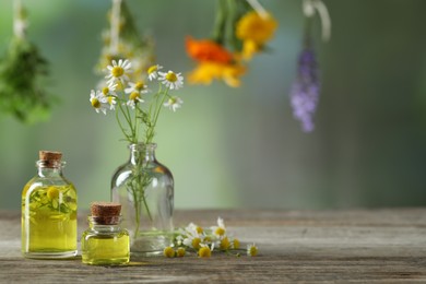 Photo of Beautiful chamomile flowers and bottles of essential oils on wooden table, space for text
