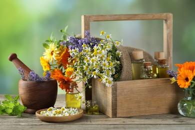 Different flowers, mint, bottles of essential oils, mortar and pestle on wooden table outdoors