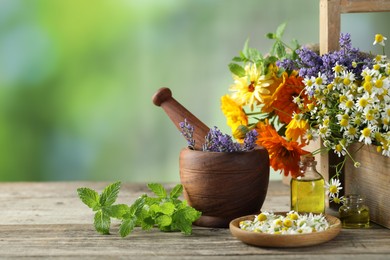 Different flowers, mint, bottles of essential oils, mortar and pestle on wooden table outdoors. Space for text