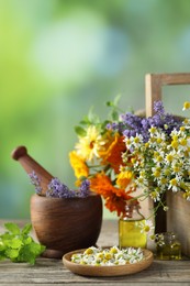 Different flowers, mint, bottles of essential oils, mortar and pestle on wooden table outdoors