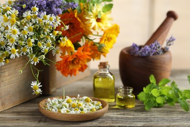 Different flowers, mint, bottles of essential oils, mortar and pestle on wooden table