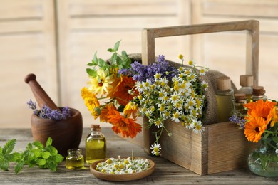 Different flowers, mint, bottles of essential oils, mortar and pestle on wooden table