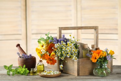 Different flowers, mint, bottles of essential oils, mortar and pestle on wooden table