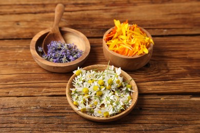 Different flowers in bowls and spoon on wooden table