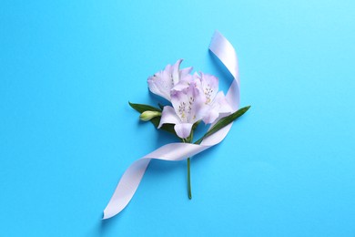 Photo of Beautiful alstroemeria flowers and ribbon on light blue background, top view