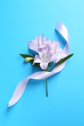 Photo of Beautiful alstroemeria flowers and ribbon on light blue background, top view