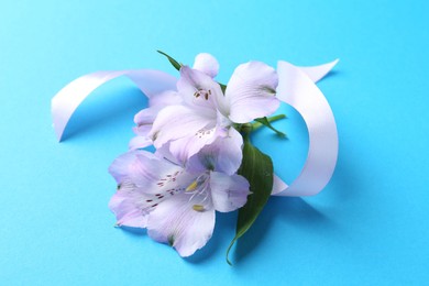 Photo of Beautiful alstroemeria flowers and ribbon on light blue background