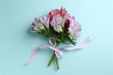 Bouquet of alstroemeria flowers and ribbon on light blue background, top view