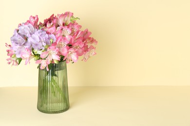 Photo of Beautiful alstroemeria flowers in vase on beige background, space for text