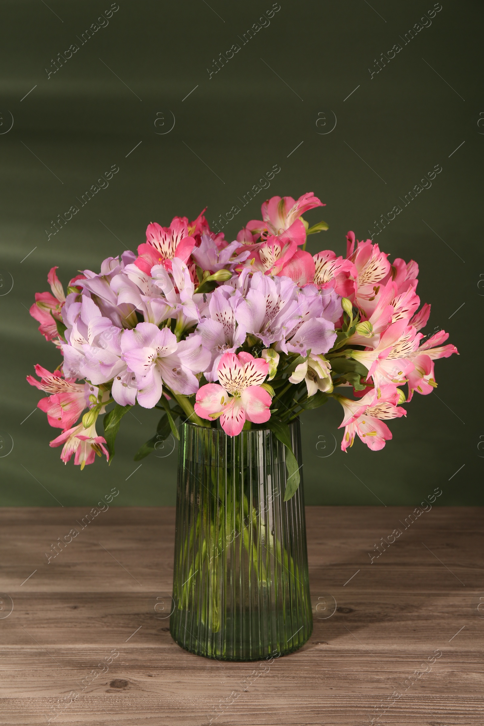 Photo of Beautiful alstroemeria flowers in vase on wooden table against green background