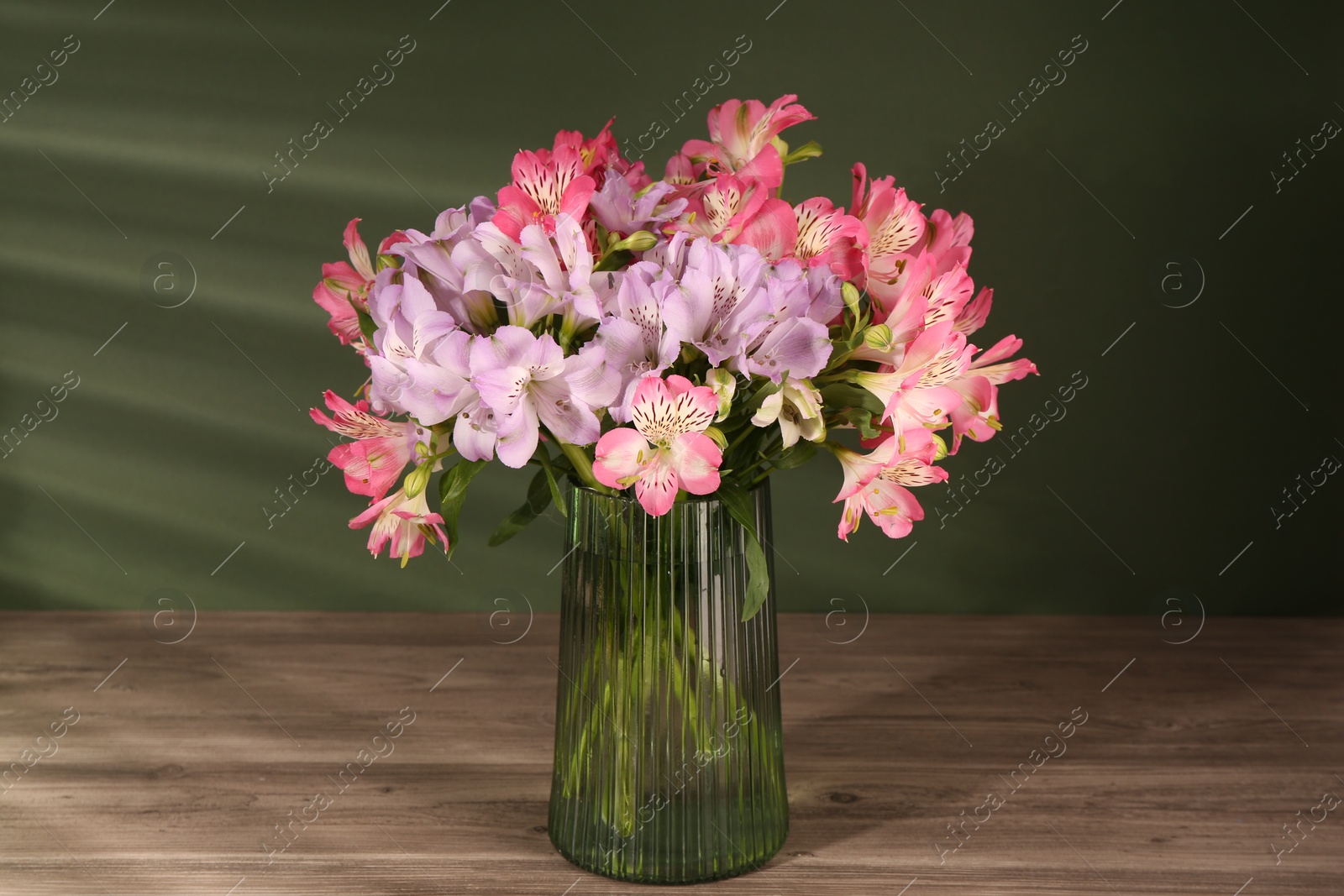 Photo of Beautiful alstroemeria flowers in vase on wooden table against green background