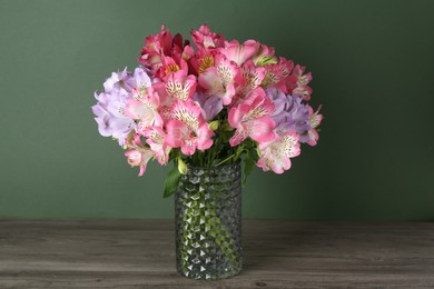 Photo of Beautiful alstroemeria flowers in vase on wooden table against green background