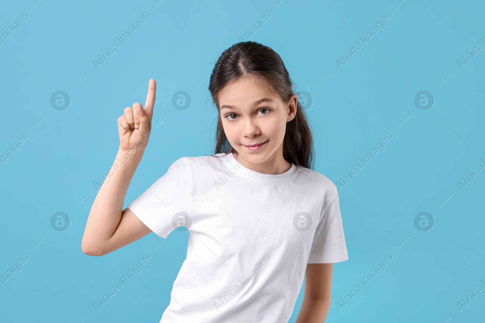 Photo of Portrait of beautiful girl pointing at something on light blue background
