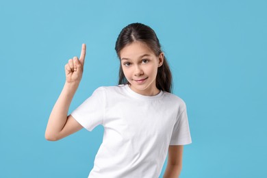 Portrait of beautiful girl pointing at something on light blue background