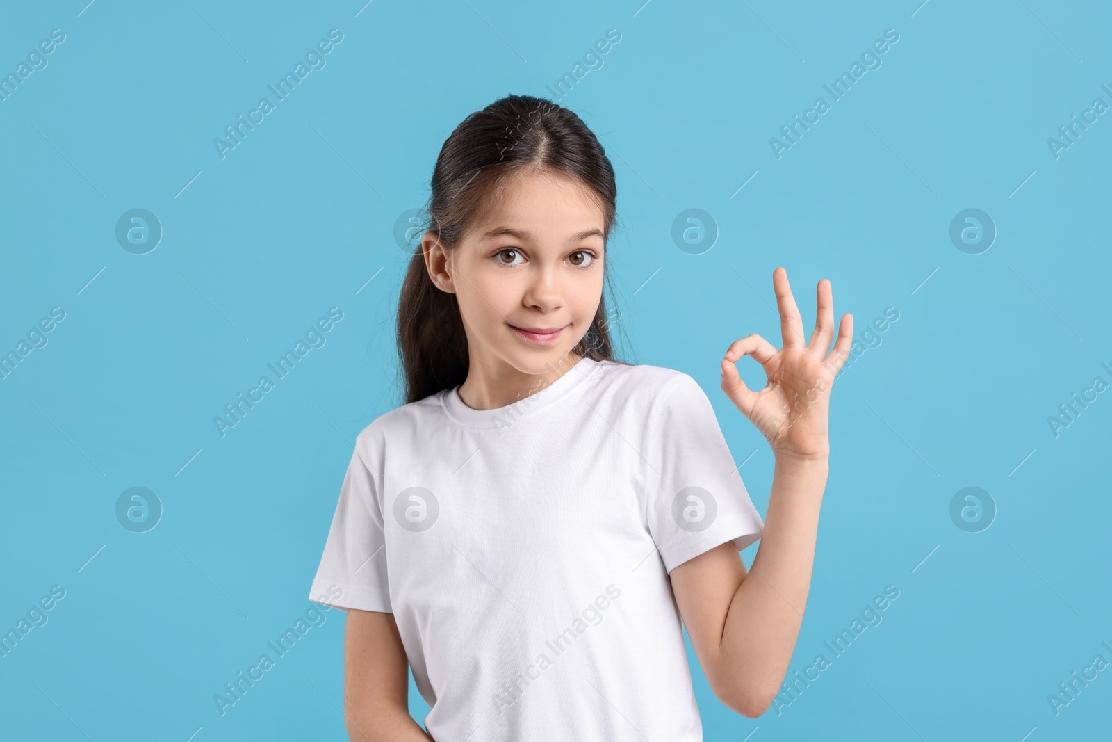 Photo of Portrait of beautiful girl showing Ok gesture on light blue background