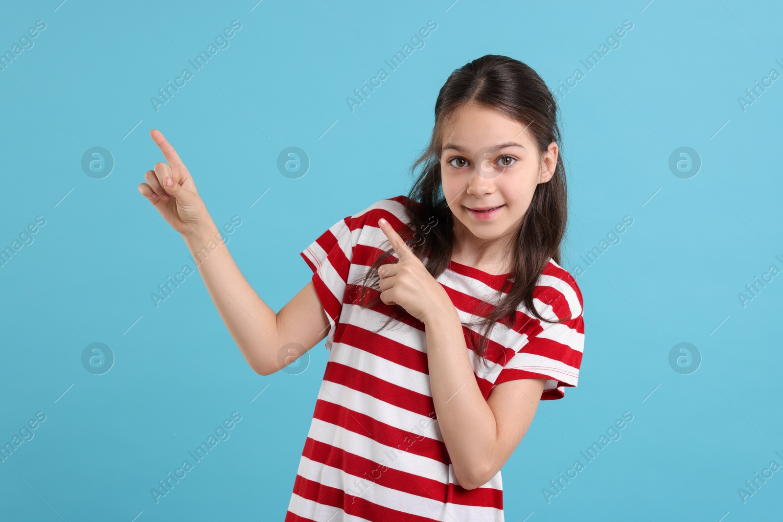 Photo of Portrait of beautiful girl pointing at something on light blue background