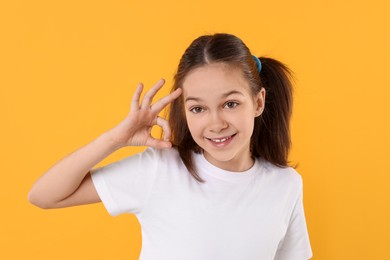 Portrait of beautiful girl showing Ok gesture on orange background