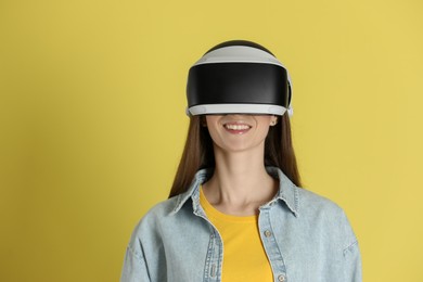 Photo of Smiling woman using virtual reality headset on yellow background, space for text