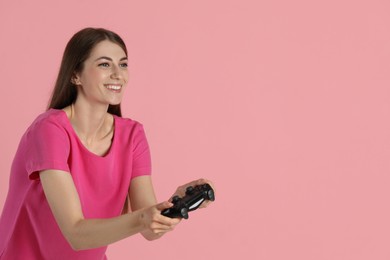 Happy woman playing video games with controller on pink background, space for text