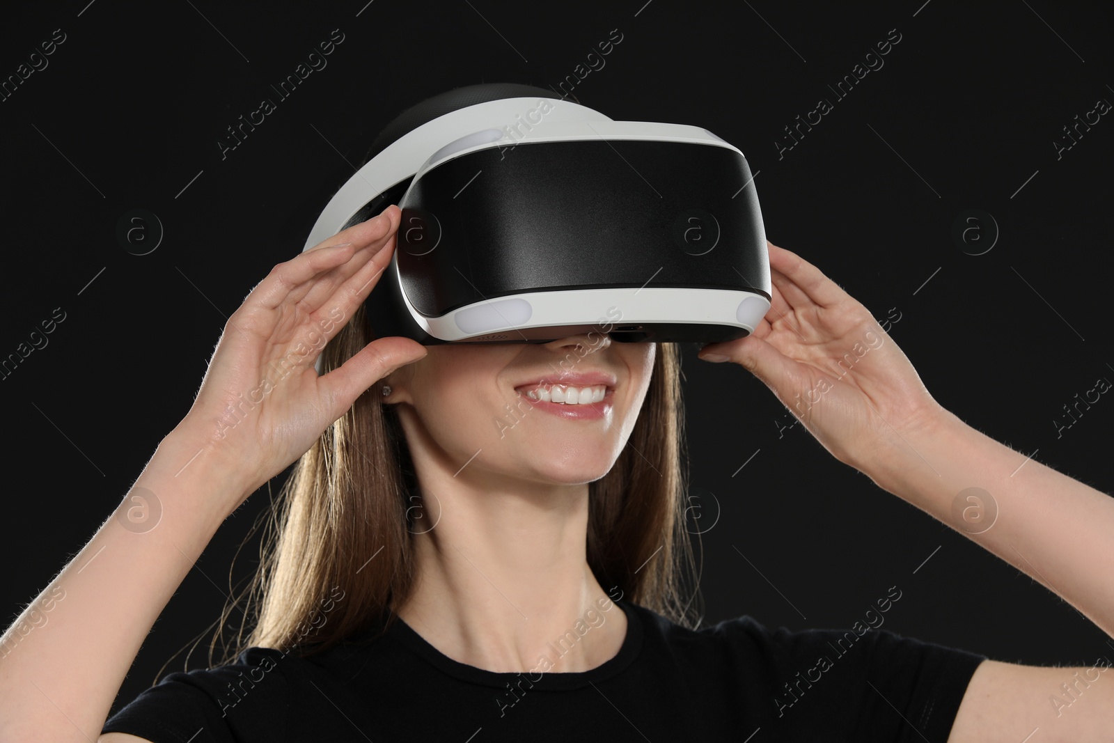 Photo of Smiling woman using virtual reality headset on black background