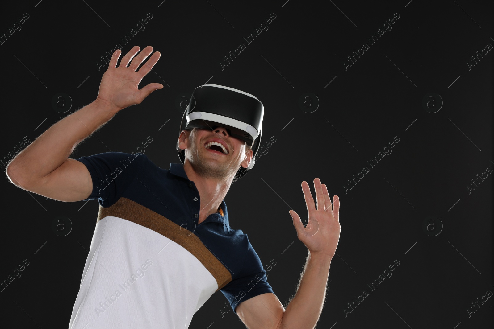 Photo of Smiling man using virtual reality headset on black background, space for text