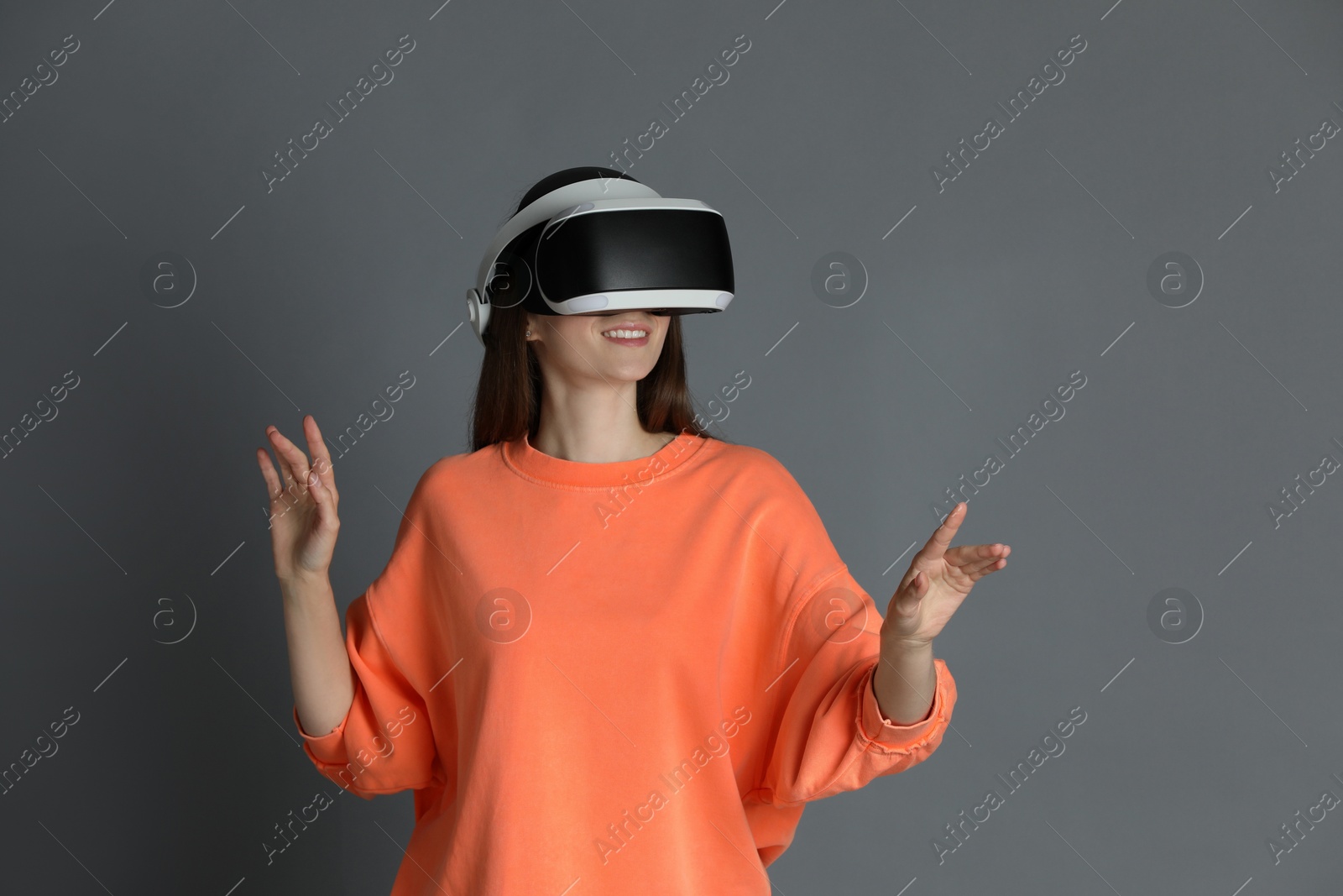 Photo of Smiling woman using virtual reality headset on gray background